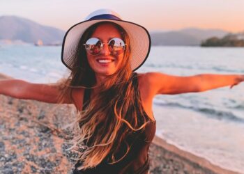 woman in black tank top and black shorts wearing black sun hat standing on beach shore