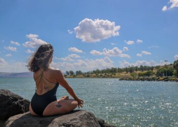 woman in black bikini sitting on rock near body of water during daytime