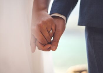 man in black suit jacket holding hands with woman in white dress